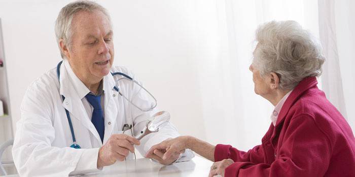 O médico examina a mão do paciente através de uma lupa.