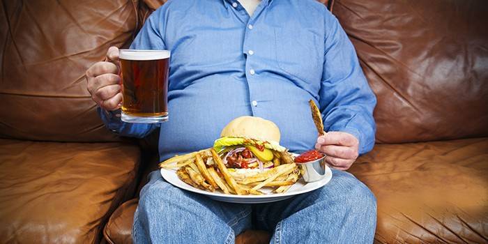 Grubas z piwem i fast foodów siedzi na kanapie