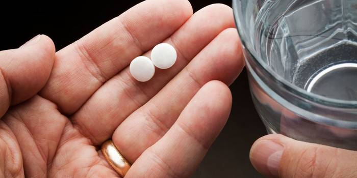 Un vaso de agua y dos pastillas en la palma de tu mano.