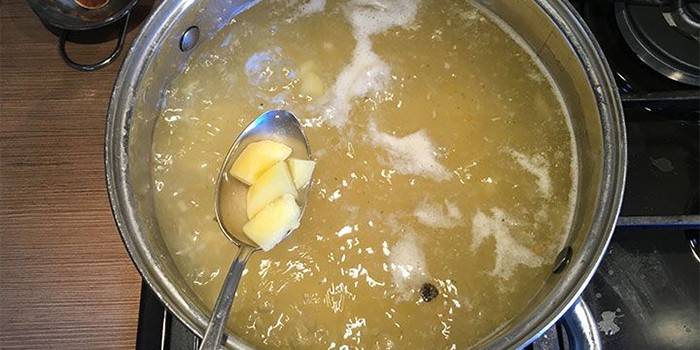 Caldo de galinha em uma panela e batatas em uma colher