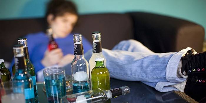 Adolescente bêbado no sofá e uma garrafa de álcool na mesa
