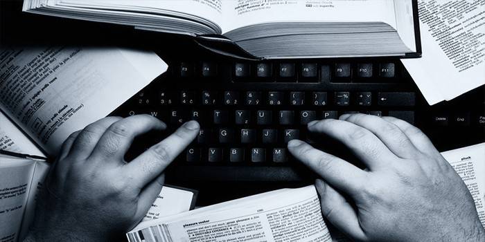 Ręce na klawiaturze laptopa i otwarte książki