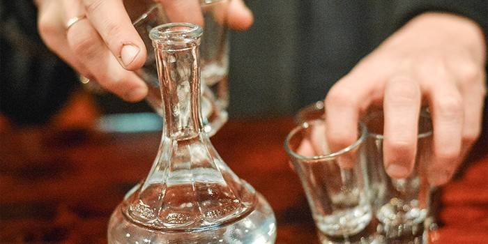 Uma garrafa com vodka e copos na mão de um homem