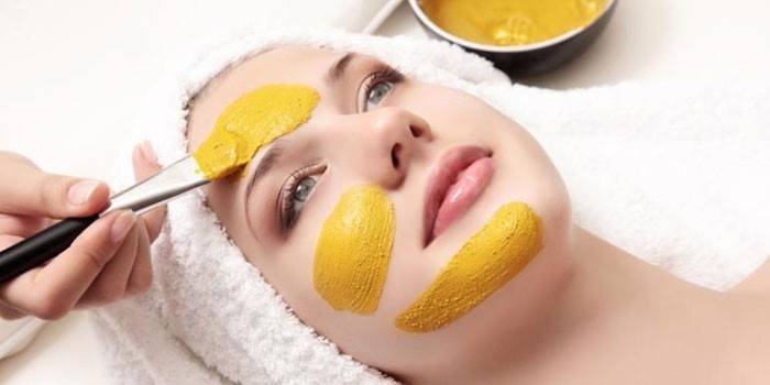 Kozmetička nanáša kurmerickú masku na tvár dievčaťa