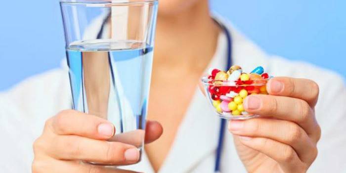 El médico sostiene en sus manos un vaso de agua y pastillas.