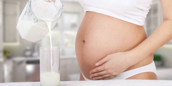 Kobieta w ciąży nalewa sfermentowane pieczone mleko do szklanki